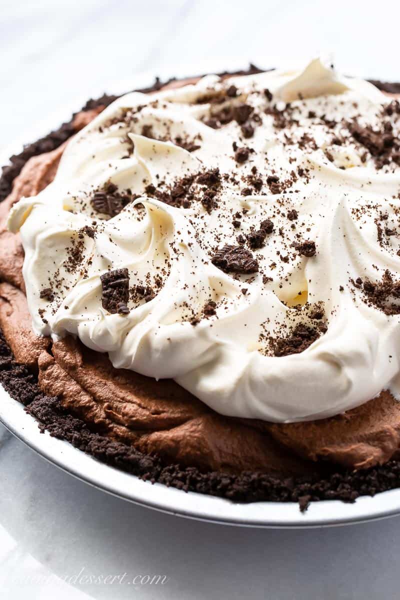 Side view of a whole chocolate icebox pie with whipped cream and crushed Oreo cookies on top