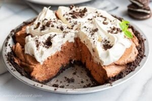 Side view of a sliced chocolate icebox pie with Oreo cookie crust topped with whipped cream and crushed cookies