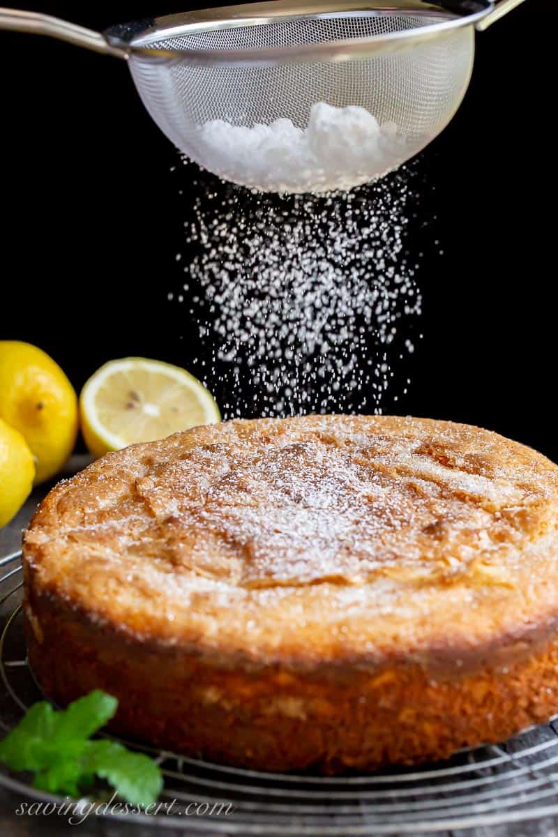 A lemon cake being dusted with powdered sugar