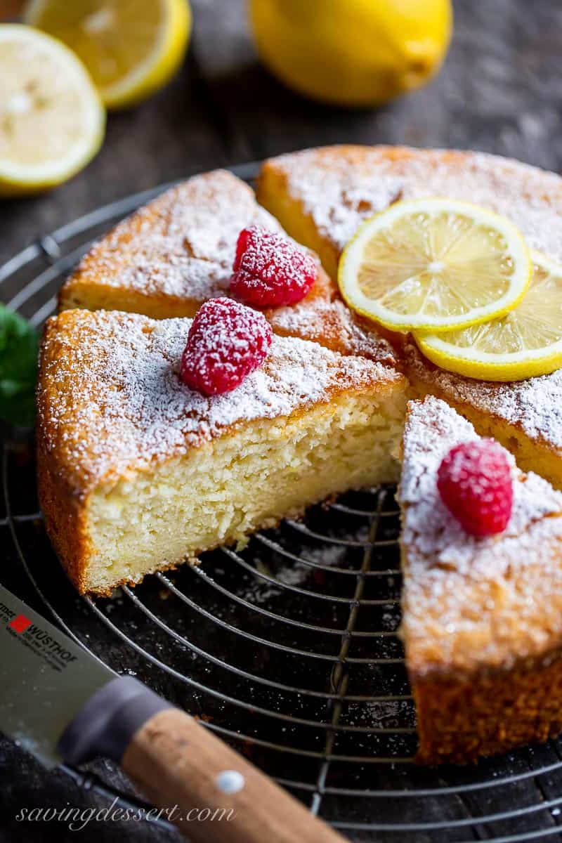 Sliced Lemon Ricotta Cake on a cooling rack topped with lemon slices and fresh raspberries