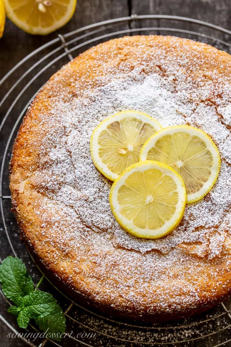 An overhead view of a one layer lemon cake topped with powdered sugar and lemon slices