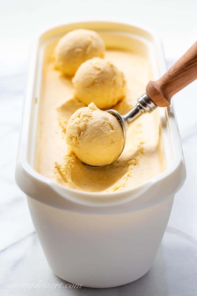 An ice cream freezer container filled with mango ice cream with scoops on top