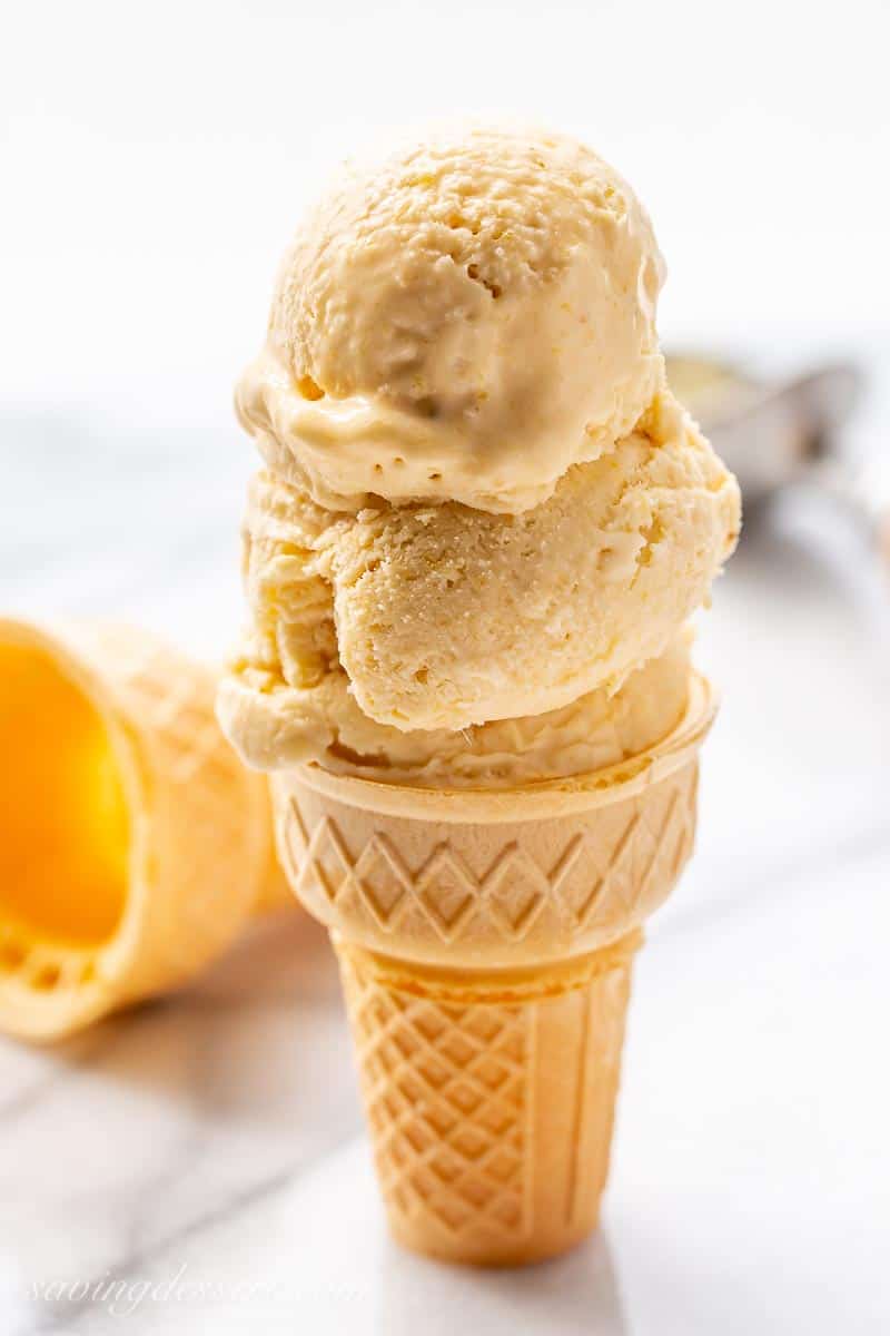 An ice cream cone topped with scoops of mango ice cream