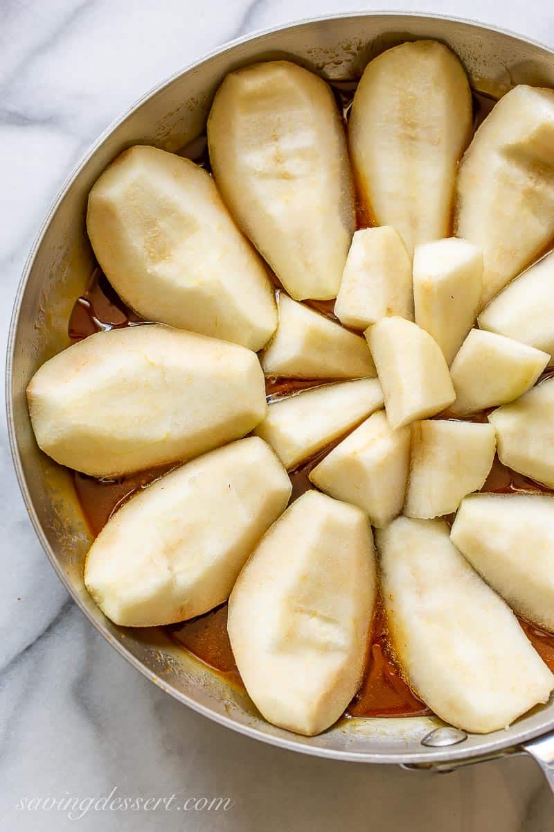 A stainless skillet filled with caramel and sliced pears