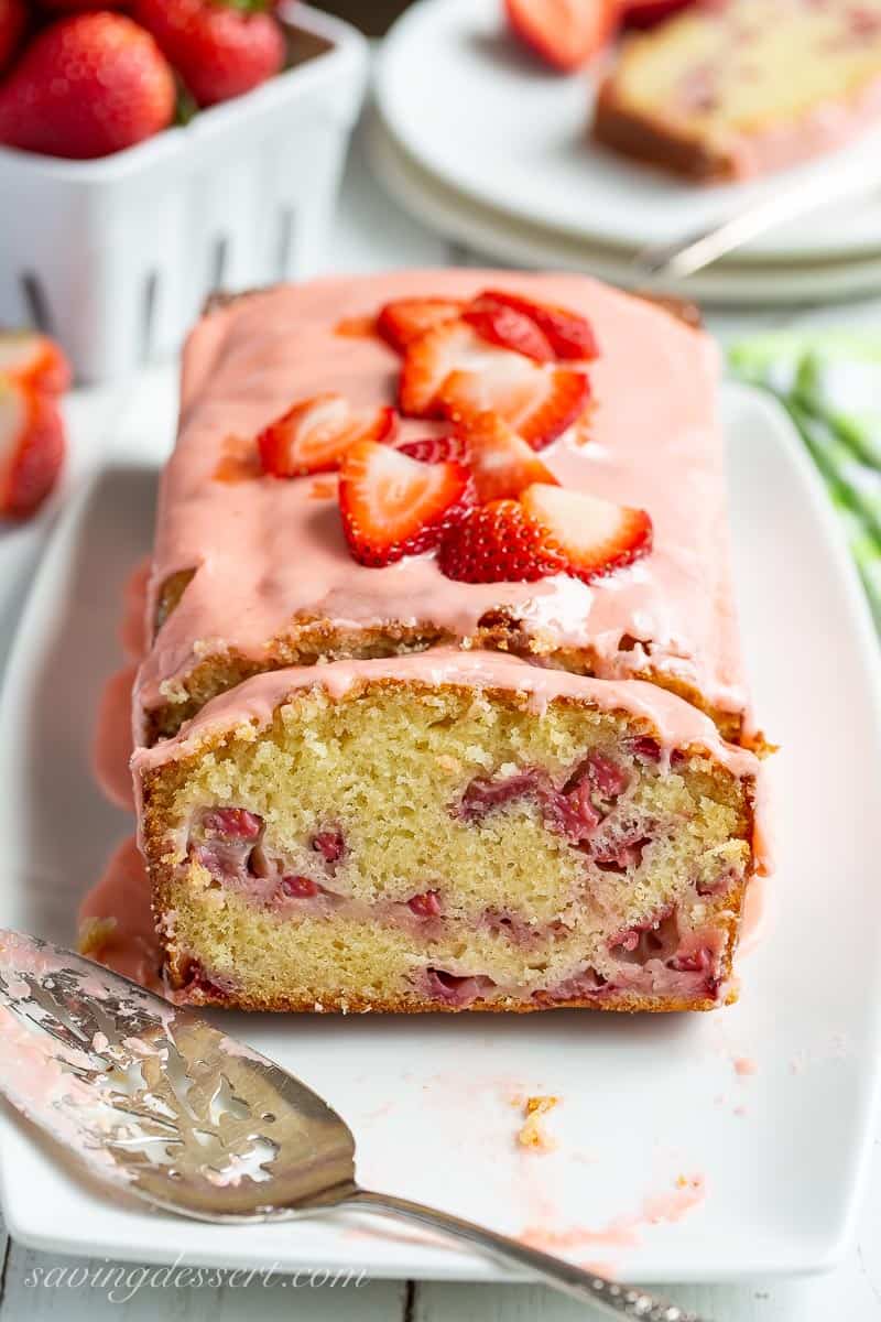 Closeup of a slice of strawberry loaf cake topped with strawberries and pink icing