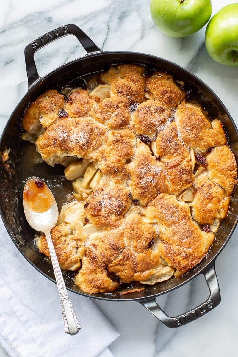 A skillet with biscuit topped apple cobbler with a spoon