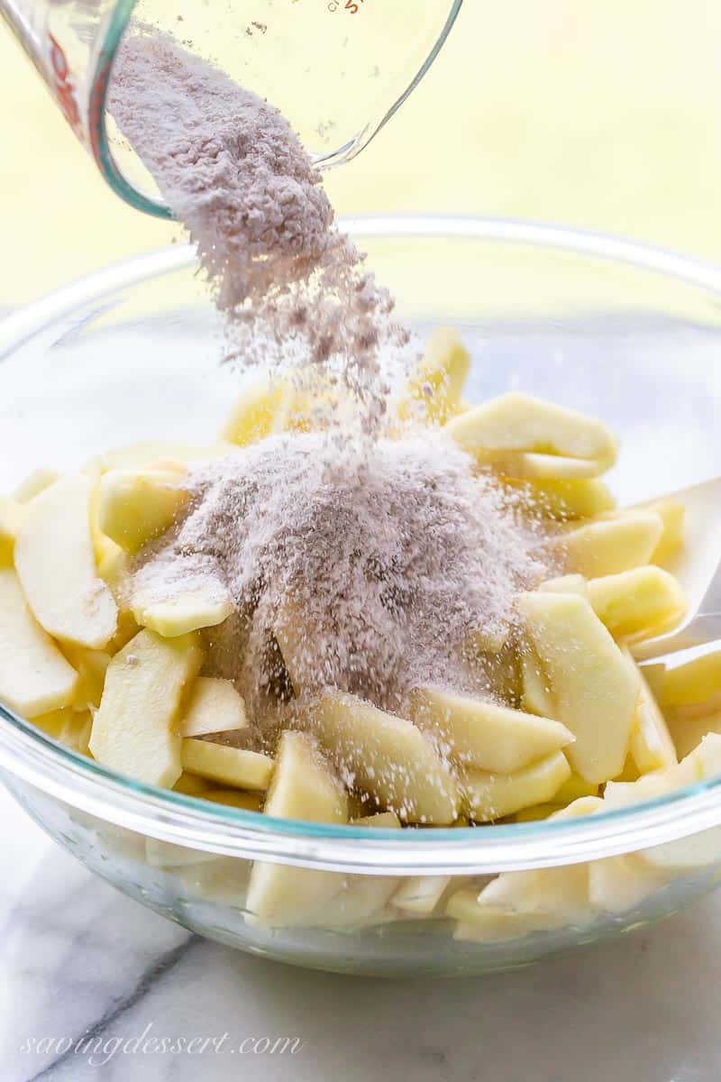 Cinnamon and sugar being poured over a bowl of sliced apples