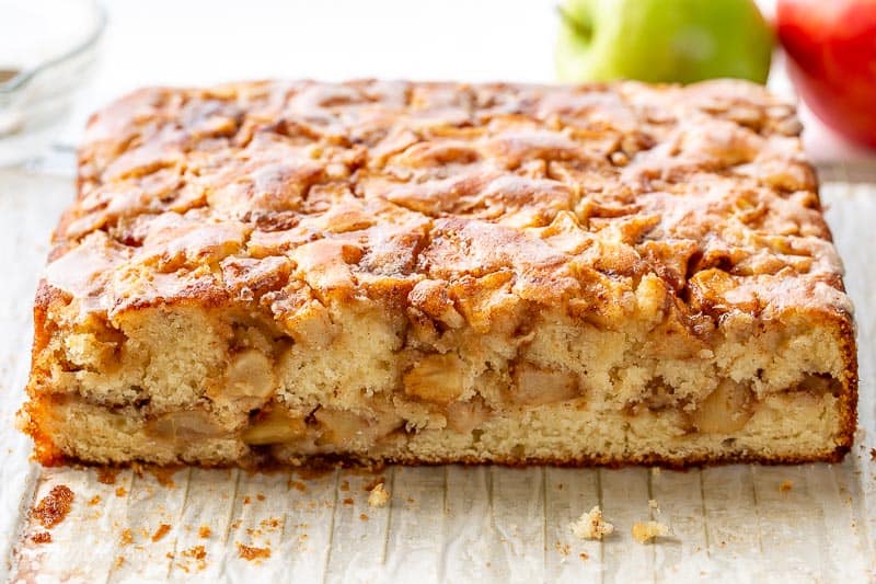 A side view of a sliced square apple fritter cake showing a ribbon of diced apples through the middle of the cake