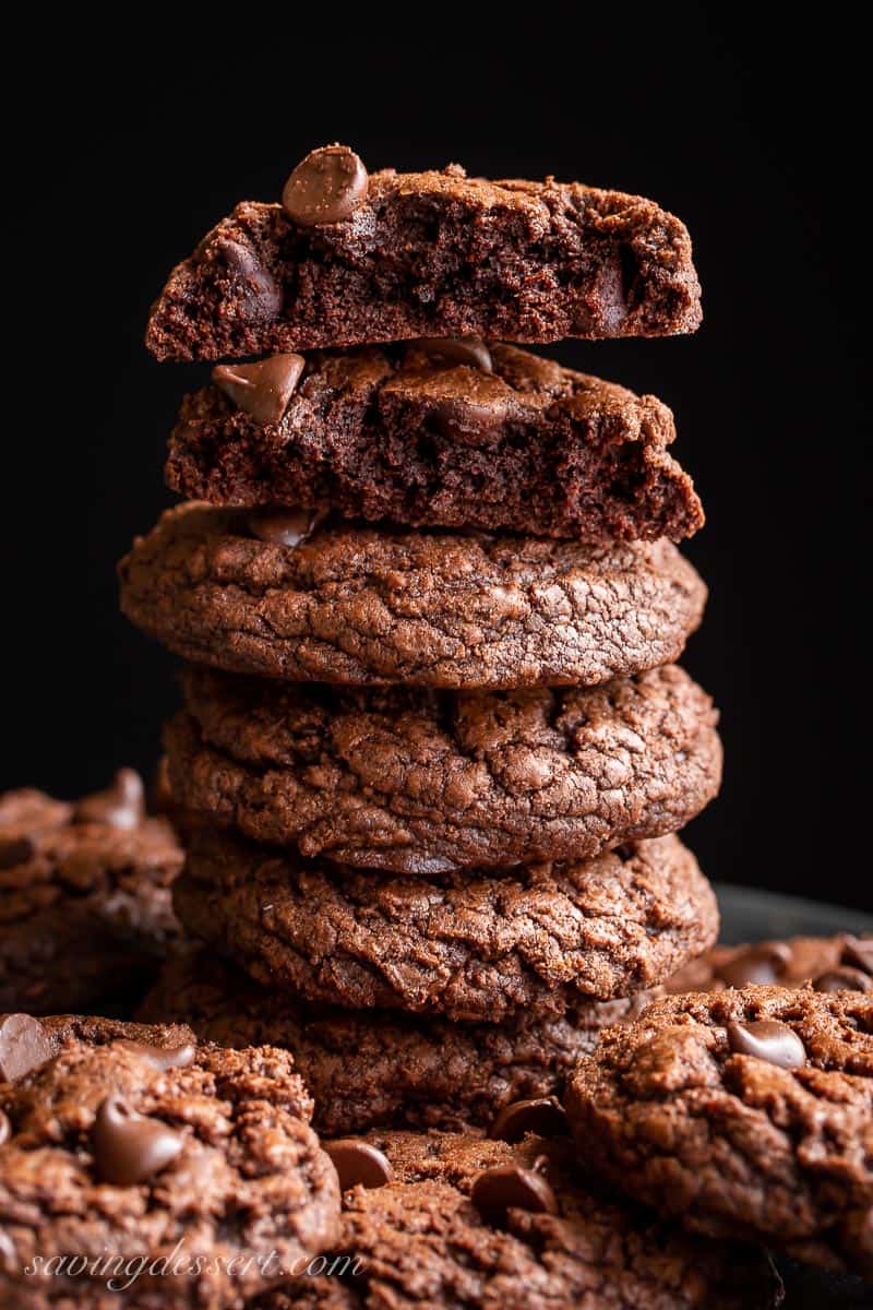 a stack of thick and fudgy chocolate brownie cookies with the top cookie broken in half to show texture