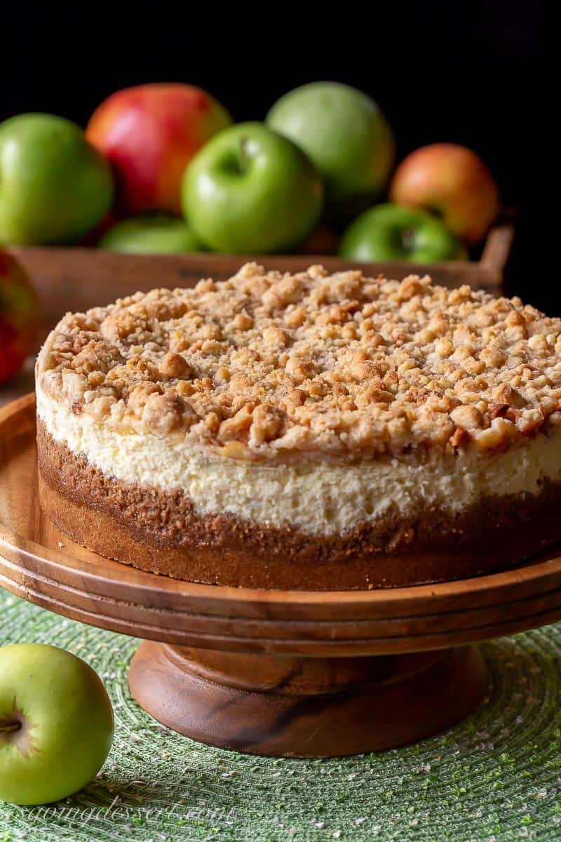 A side view of an apple cheesecake on a wooden cake stand