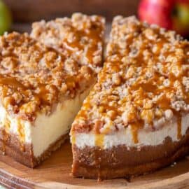 Sliced apple cheesecake with a crumble topping on a wood cake stand