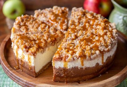 Sliced apple cheesecake with a crumble topping on a wood cake stand