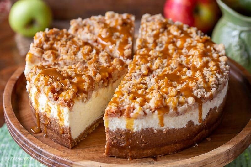 Sliced apple cheesecake with a crumble topping on a wood cake stand