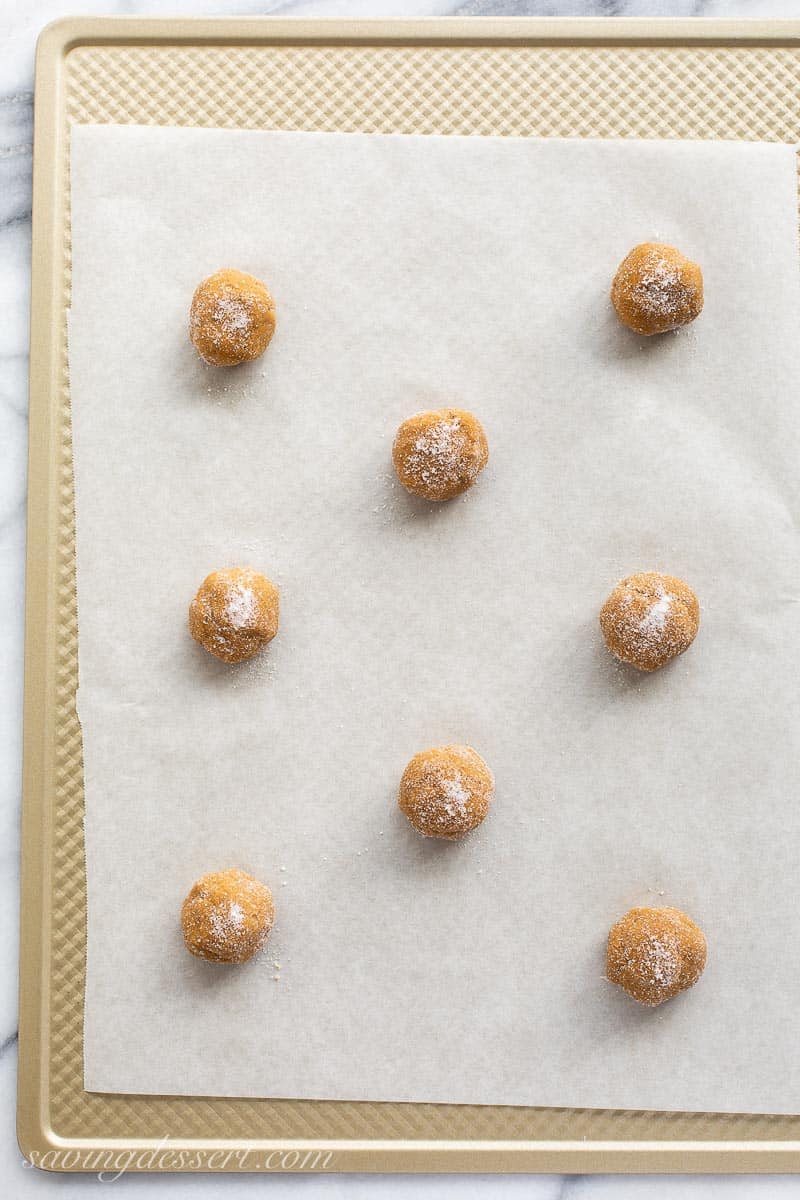 A baking sheet of rolled cookie dough balls covered in granulated sugar