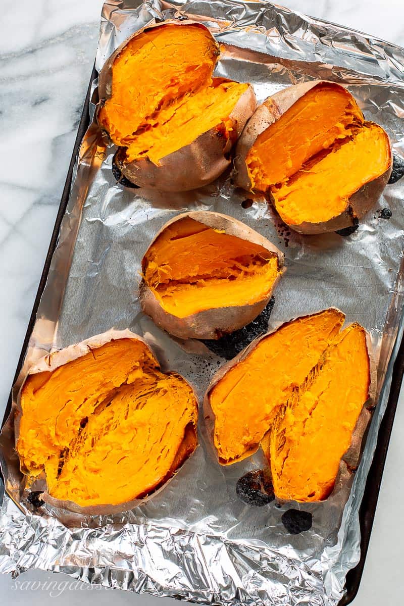 Overhead view of a baking pan with baked sweet potatoes split down the middle
