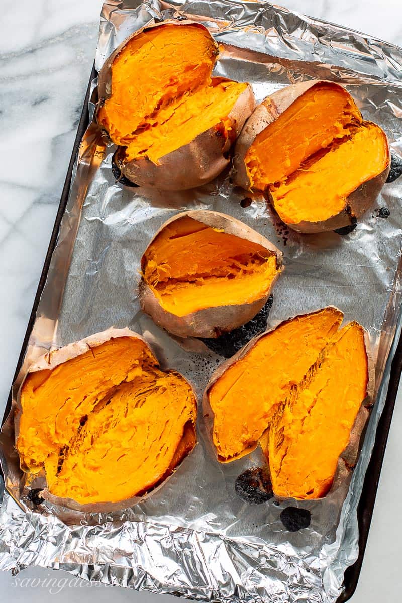 Overhead view of a baking pan with baked sweet potatoes split down the middle