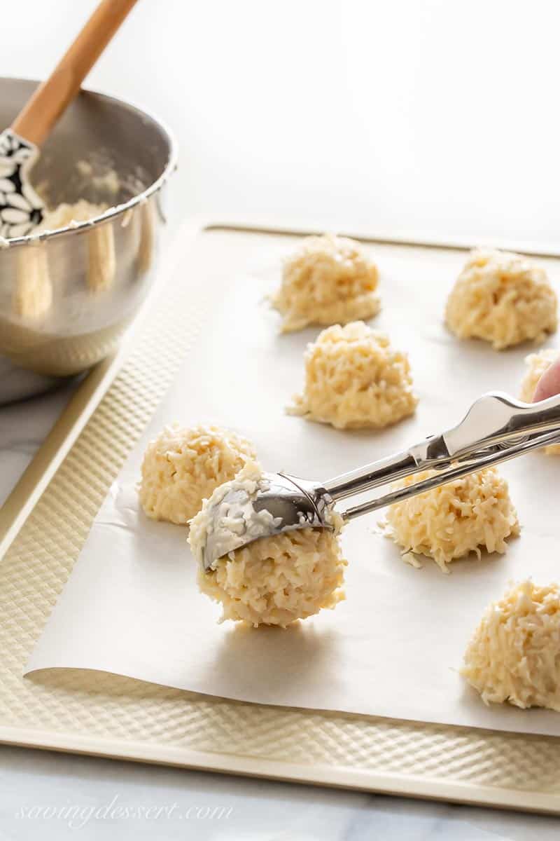 A cookie scoop dropping a mound of unbaked coconut macaroon dough on a baking sheet