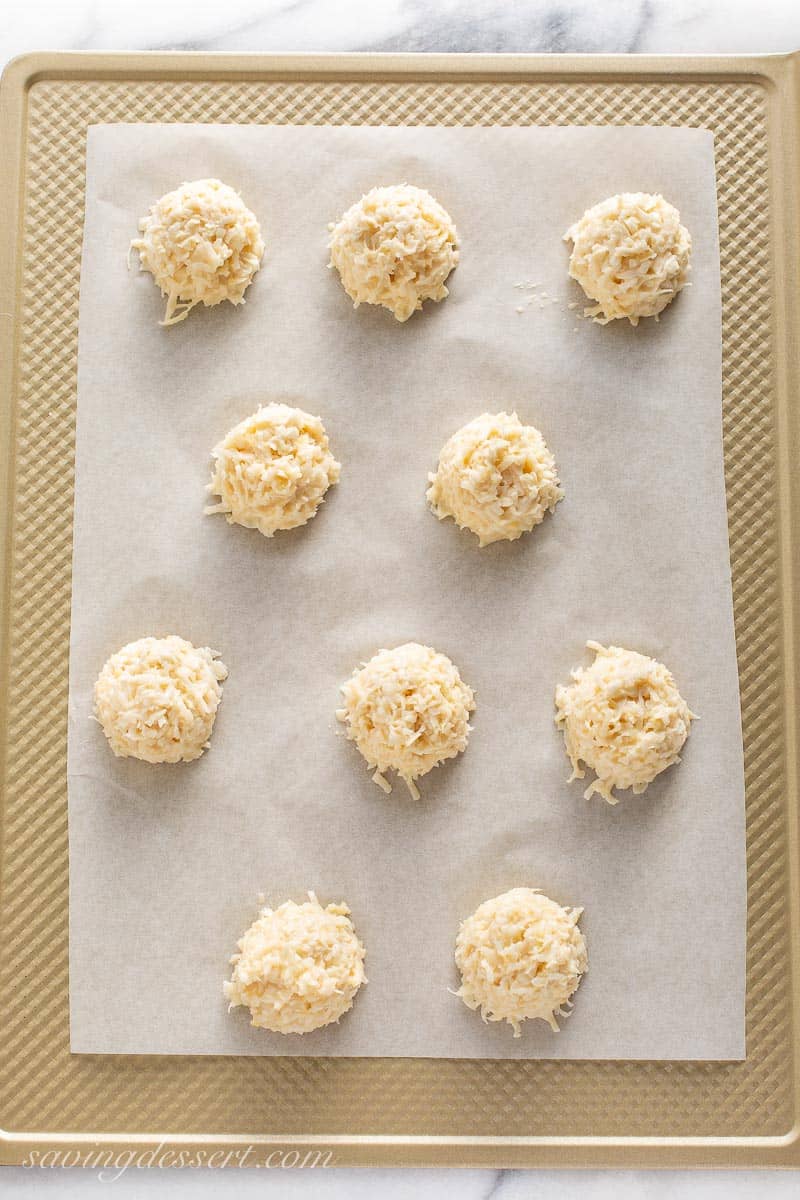 Unbaked mounds of macaroon dough on a parchment lined baking sheet