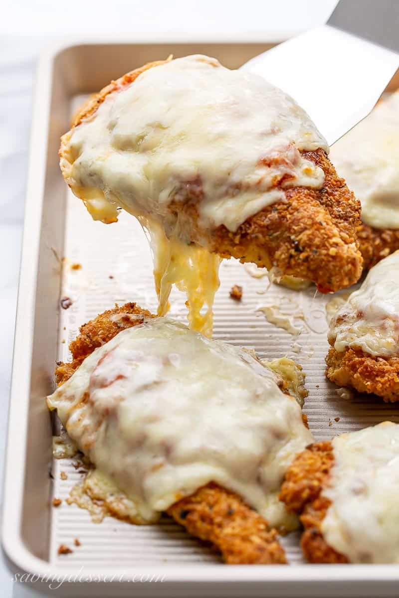 A spatula lifting a cheesy piece of chicken parmesan from a baking tray