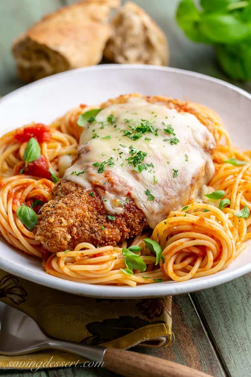 A bowl of Chicken Parmesan served over spaghetti noodles with marinara sauce