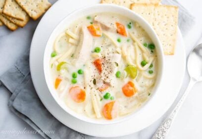 Overhead view of a bowl of creamy chicken noodle soup with carrots, peas and celery served with crackers