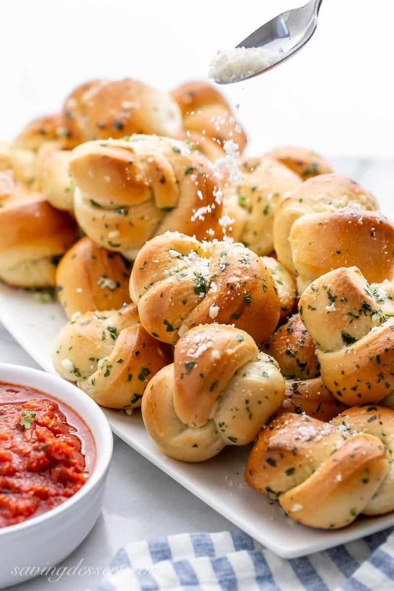 Buttery garlic knots on a platter being dusted with grated Parmesan cheese