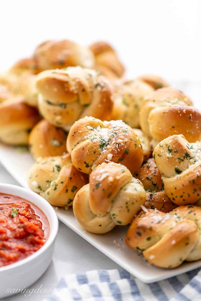 Buttery Garlic Knots on a platter with a bowl of marinara