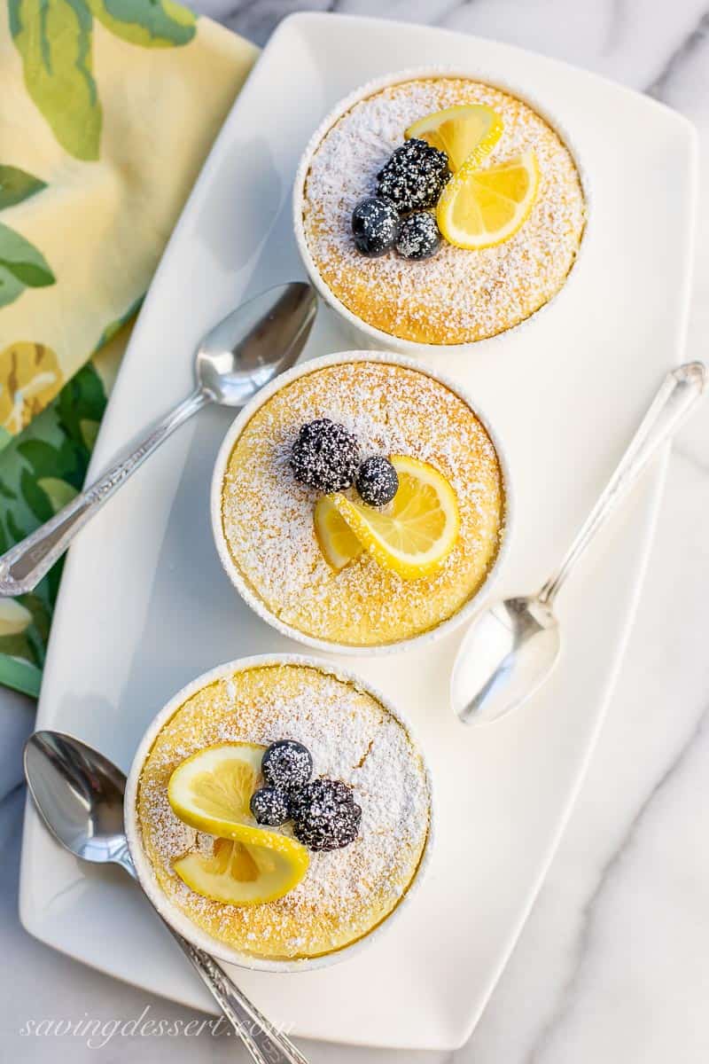 Lemon Pudding Cakes on a platter with a slice of lemon, blueberries and a blackberry on top