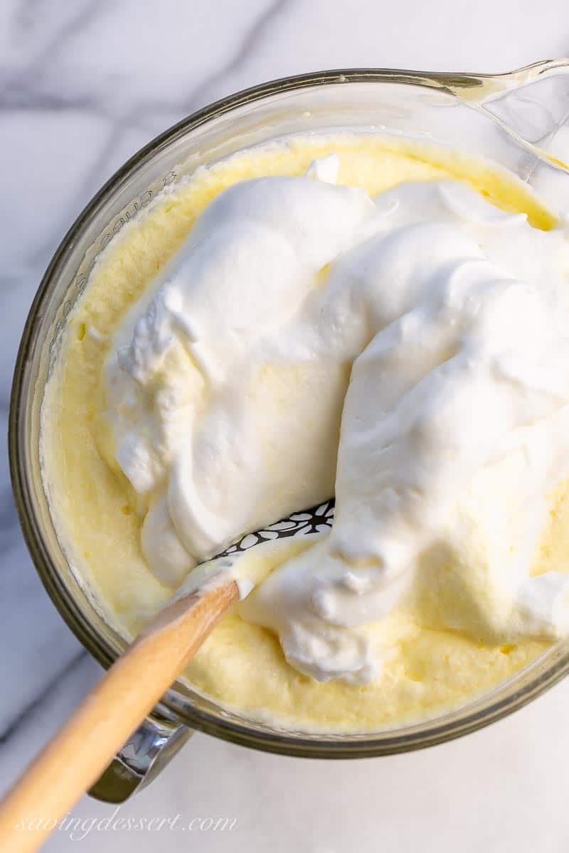 Fluffy egg whites being folded into a bowl of cake batter with a spatula