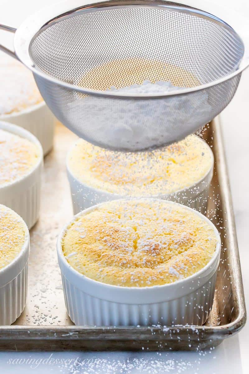 Individual cakes baked in ramekins being dusted with a sieve of powdered sugar