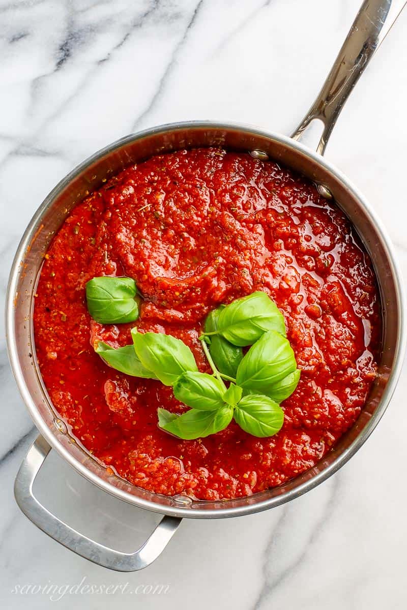 A large saucepan filled with tomato sauce and fresh basil