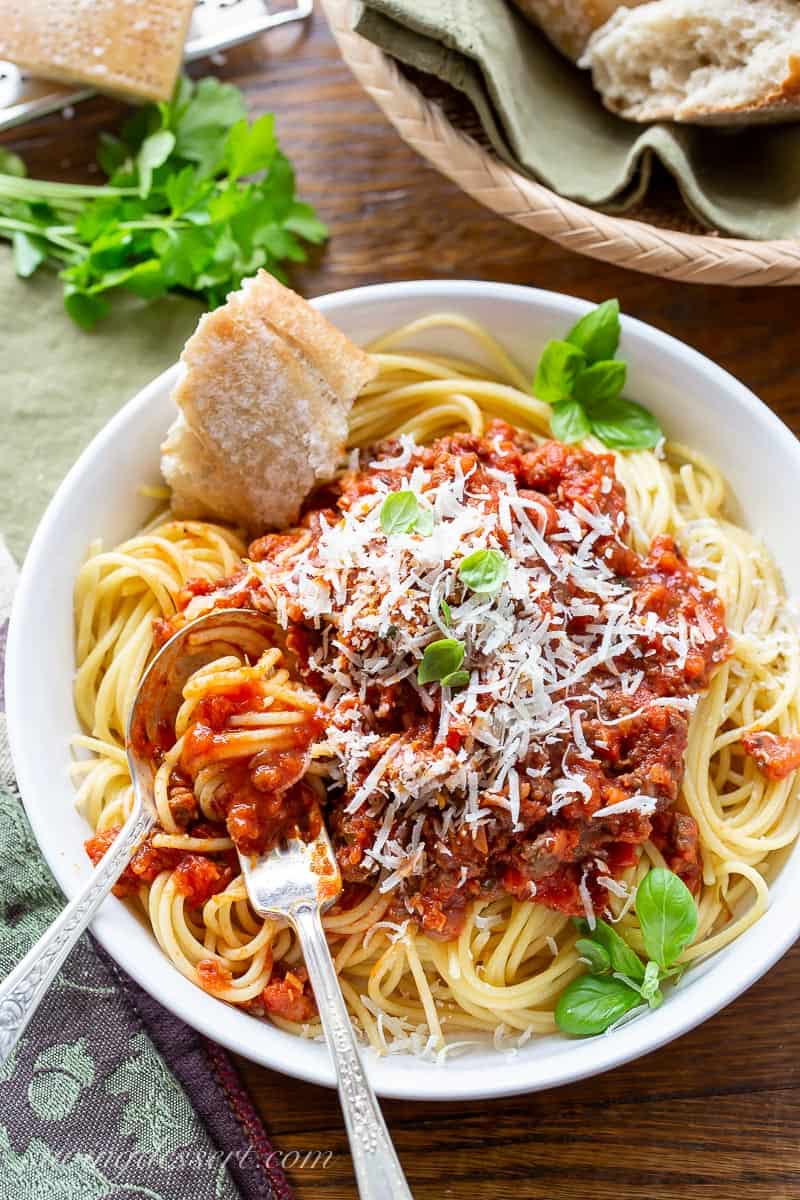 A big bowl of pasta topped with meaty spaghetti sauce with a hunk of crusty bread