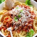 A bowl of spaghetti covered with meaty spaghetti sauce topped with basil and fresh Parmesan
