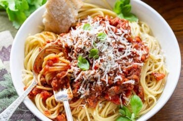 A bowl of spaghetti covered with meaty spaghetti sauce topped with basil and fresh Parmesan