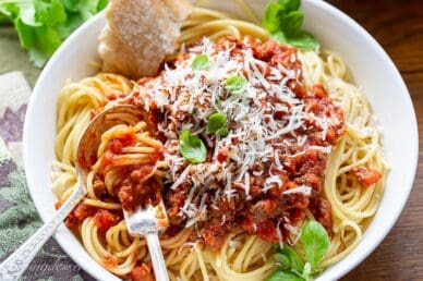 A bowl of spaghetti covered with meaty spaghetti sauce topped with basil and fresh Parmesan