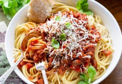 A bowl of spaghetti covered with meaty spaghetti sauce topped with basil and fresh Parmesan