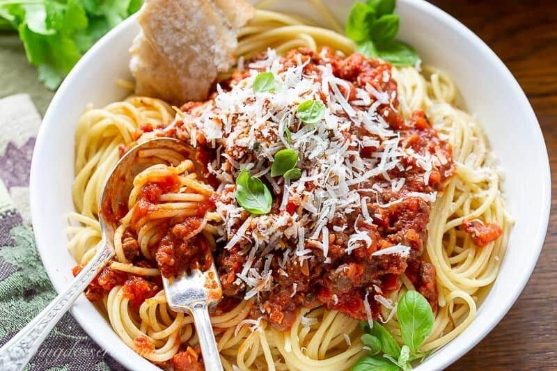 A bowl of spaghetti covered with meaty spaghetti sauce topped with basil and fresh Parmesan