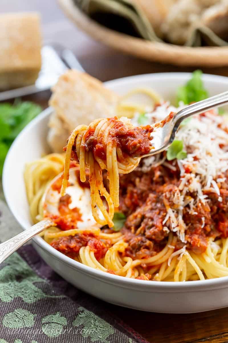 A fork full of pasta noodles drenched in a meaty tomato sauce over a bowl