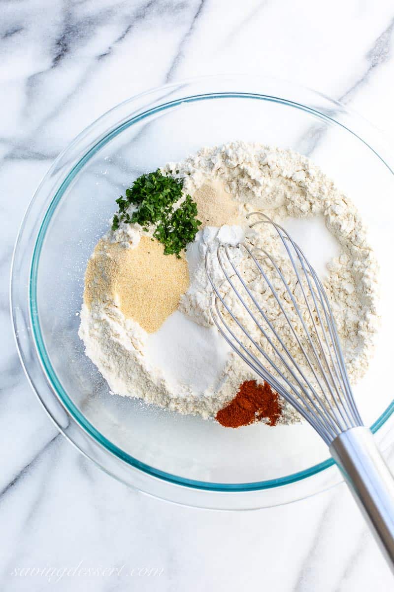 A bowl of flour, herbs and spices with a whisk