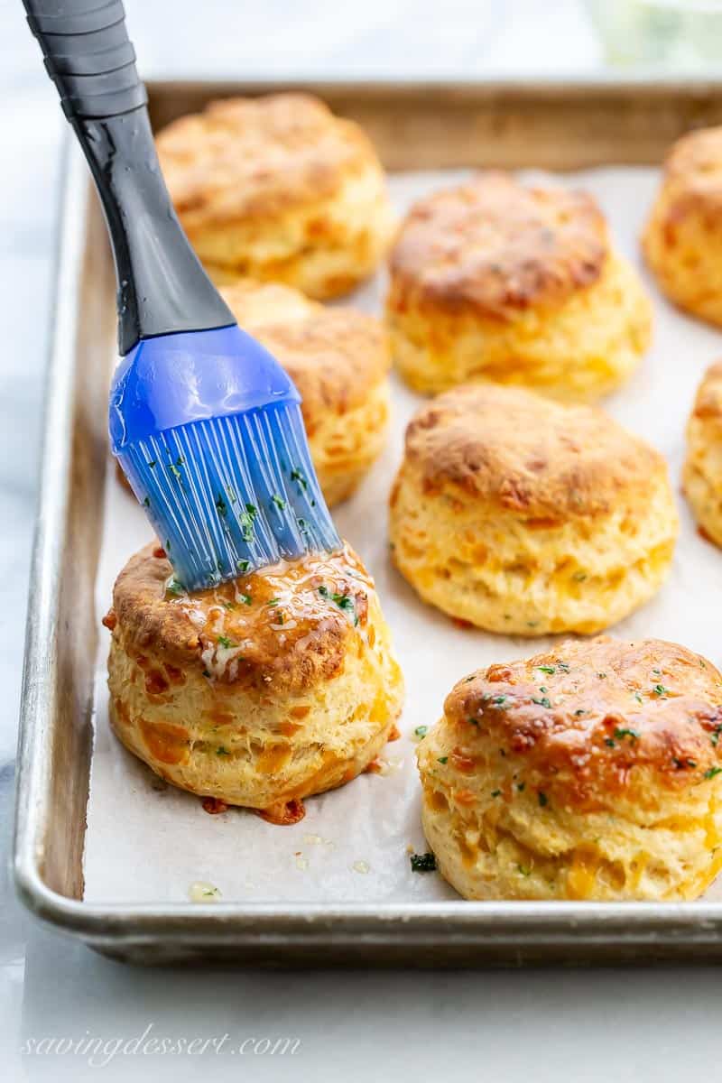 Cheddar bay biscuits on a baking pan being brushed with melted butter