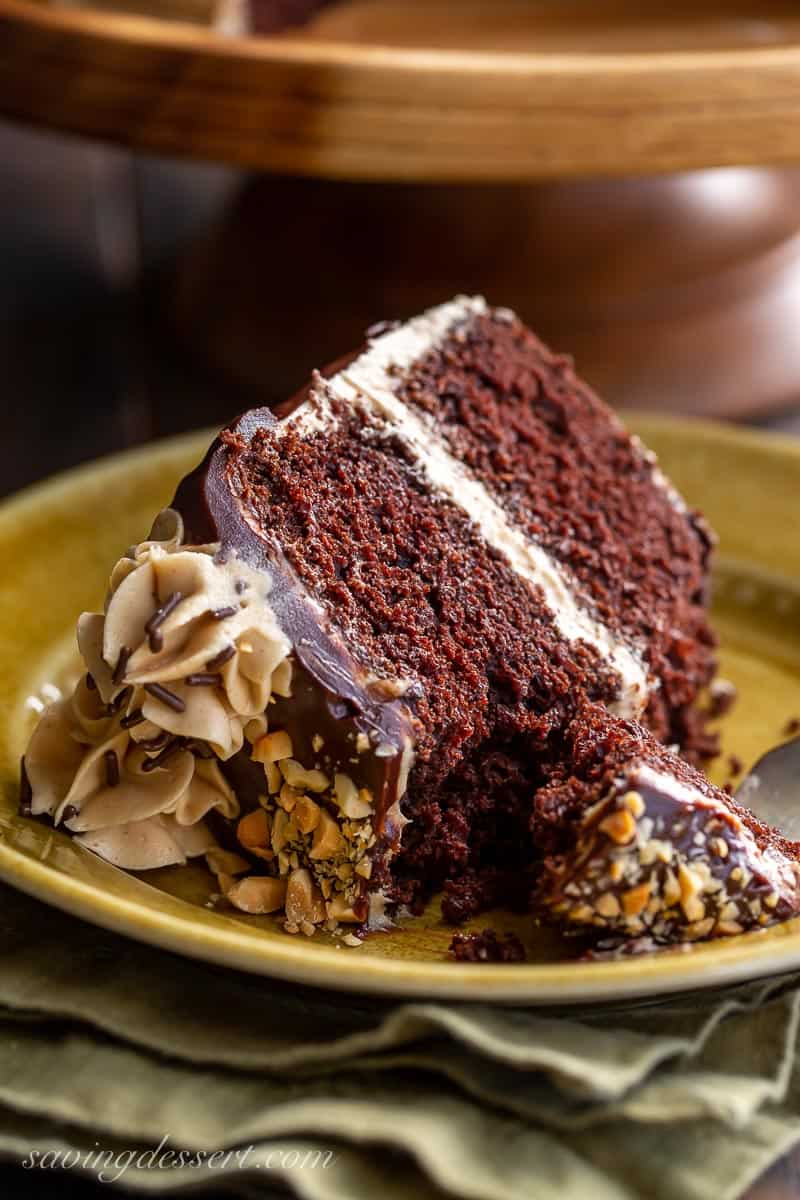 A side view of a thick slice of chocolate cake with peanut butter frosting and a fork