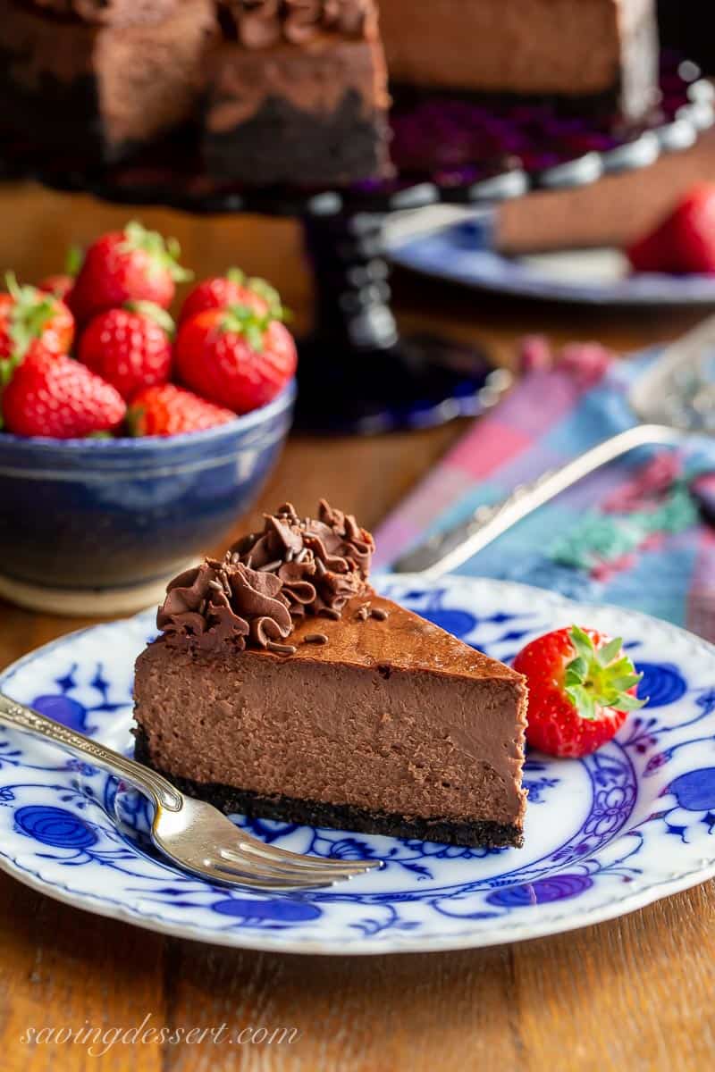A slice of chocolate cheesecake on a blue plate with strawberries on the side