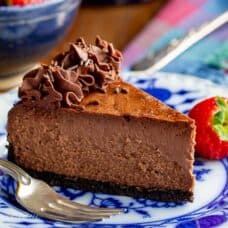Chocolate cheesecake with a swirl of whipped chocolate ganache on a plate with strawberries