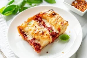 A slice of pizza on a white plate with fresh basil