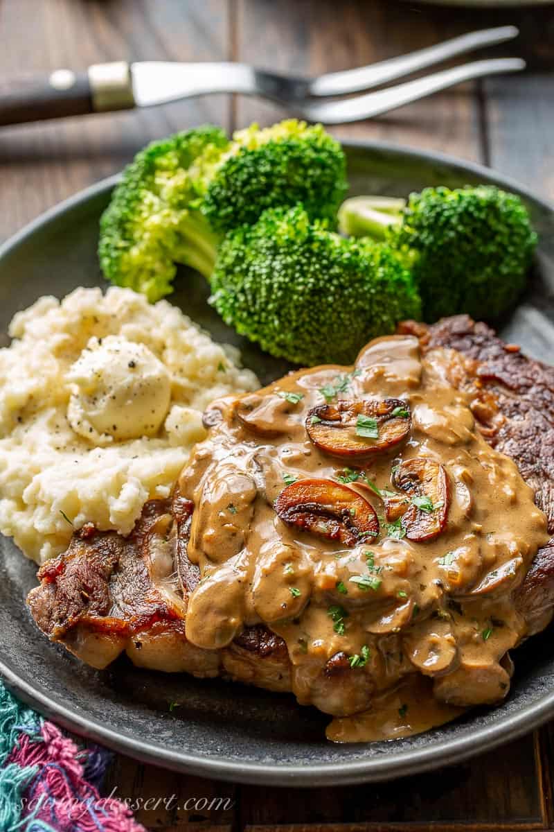 Ribeye steak, mashed potatoes and broccoli on a plate covered with mushroom sauce