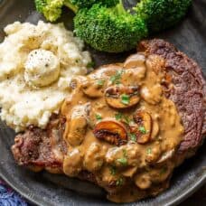 A ribeye steak covered in mushroom sauce served with broccoli and potatoes