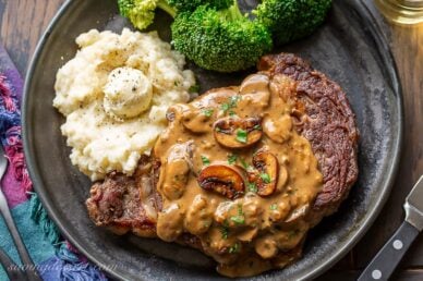 A ribeye steak covered in mushroom sauce served with broccoli and potatoes