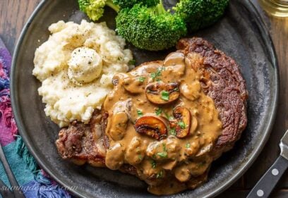 A ribeye steak covered in mushroom sauce served with broccoli and potatoes