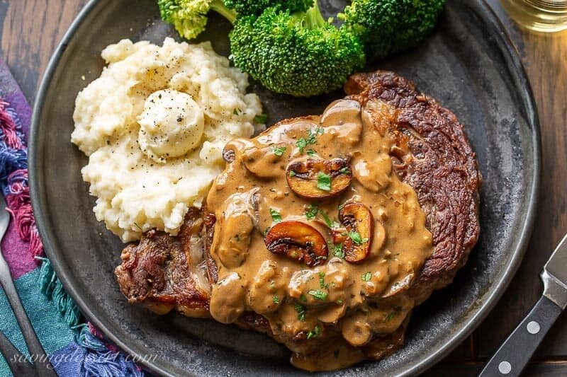 A ribeye steak covered in mushroom sauce served with broccoli and potatoes