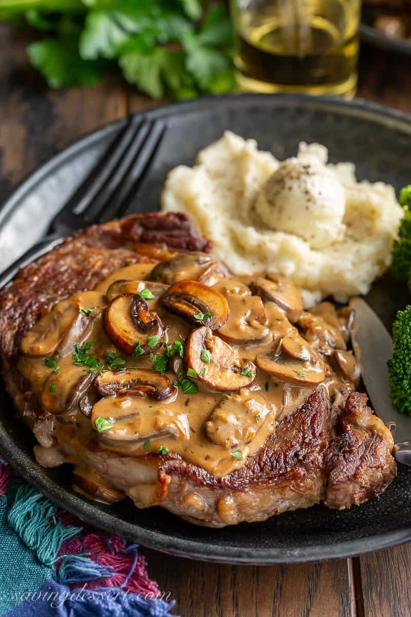A steak on a plate covered with mushroom sauce and served with mashed potatoes